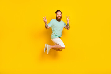 Full body photo of carefree jumping hipster chilling guy red hair beard show v-sign overjoyed peace symbol isolated on yellow color background
