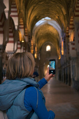 Obraz na płótnie Canvas Middle-aged woman takes a photo with her mobile phone in the interior of a cathedral