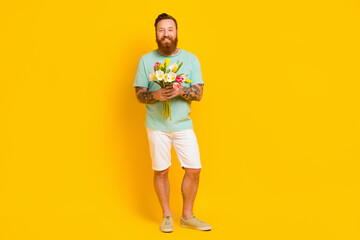 Photo of cheerful romantic man hold give flowers going meeting 8 march empty space isolated on yellow color background