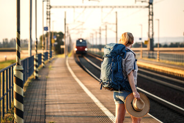 Traveler with backpack standing at railroad station platform and looking at arriving train