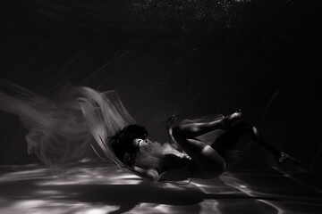 Fototapeta na wymiar Underwater shoot of beautiful woman in white flying transparent dress relaxing in water in sunbeams.