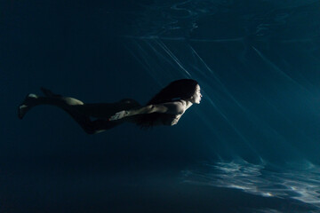 Underwater shoot of beautiful woman with long hair swimming in water in sunbeams.