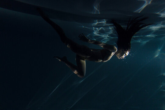 Underwater shoot of beautiful woman with long hair dancing in water in sunbeams.