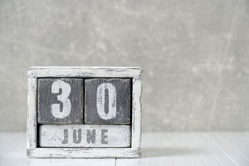 Calendar for June 30, made wooden cubes, against light concrete wall.With an empty space for your text.