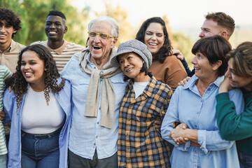Group of multigenerational people having fun hugging each other outdoor - Crowd of multiracial friends enjoy day at city park