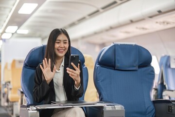 Young woman sitting with phone video call on the aircraft seat near the window during the flight in the airplane