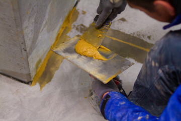 The professional is skillfully filling the expansion joints with epoxy mortar using a trowel and putty knife, ensuring that the material is spread evenly and completely fills the joint