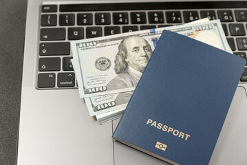 Blue-covered copy space passport on laptop keyboard with U.S. cash dollars on close up. Online travel booking and remote work concept.