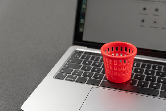 Concept of deleting files and cleaning up information garbage. Miniature toy trash can on laptop keyboard. Cleaning laptop
