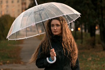 Sad girl with umbrella in autumn park. November seasonal portrait. Young woman with long brown heir...