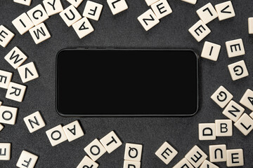 Black smartphone with blank screen in frame made of white letters of English alphabet on gray background. Copy space,