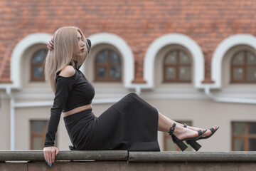 Young attractive woman with long blonde hair wears black clothes long skirt and heels. Portrait of...