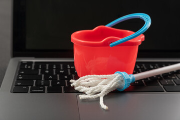 Toy bucket and mop on laptop keyboard. Order cleaning service online. Cleaning and maintenance of...