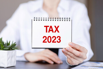 Text TAX 2023 on a notebook in the hands of a businesswoman.