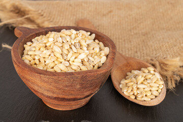 Pearl barley with wooden cup, spoon and jute napkin on slate stone, macro.