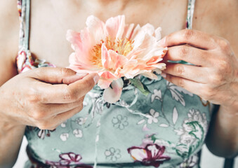 Mature woman wearing floral print dress holding beautiful peony flower. No face visible. Female power and sensitivity. Thyroid and health problems - 587008823
