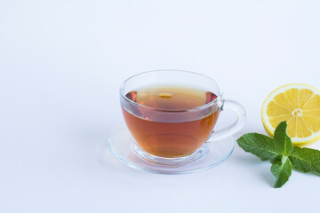 Black tea in the glass cup, lemon and mint on the white background. Copy space. Close-up.