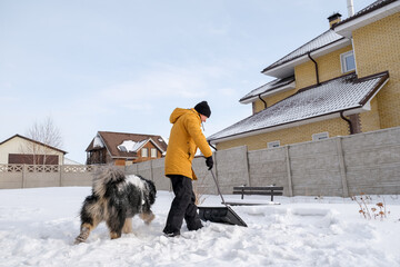 Man removing snow from sidewalk after snowfall. Portrait of man with dog during winter time