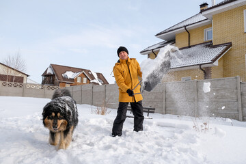 Man removing snow from sidewalk after snowfall. Portrait of man with dog during winter time