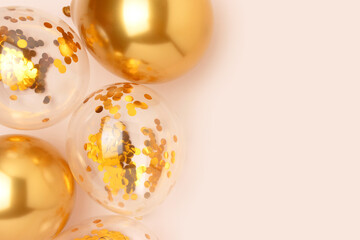 Gold colored inflatable balloons with confetti inside on a beige background. Creative concept with place for text. Selective focus.