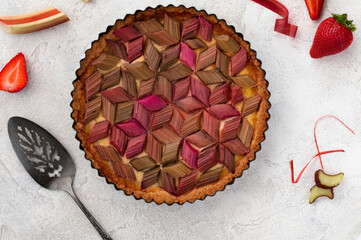 Rhubarb custard tart with geometric pattern and strawberry jam on a light stone table. Spring and...