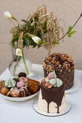 Easter traditional cakes, desserts and sweets on the table with white tablecloth and glass vase with flowers on it on the background of beige wall