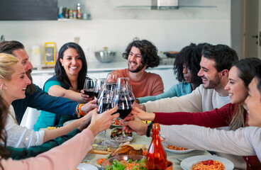 young people holding wine glasses and toasting while celebrating together at table during dinner party