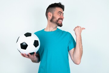 Charming Young man holding a ball over white background looking at copy space having advertisements