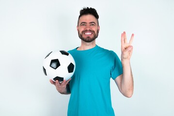 Young man holding a ball over white background showing and pointing up with fingers number three...