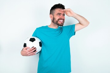 Young man holding a ball over white background very happy and smiling looking far away with hand...