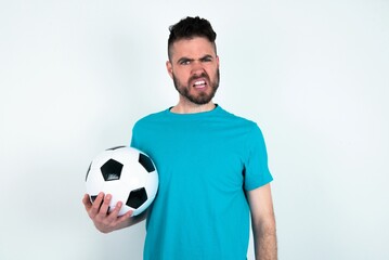 Portrait of dissatisfied Young man holding a ball over white background smirks face, purses lips and looks with annoyance at camera, discontent hearing something unpleasant