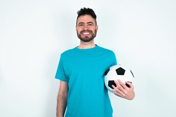 Young man holding a ball over white background with nice beaming smile pleased expression. Positive emotions concept