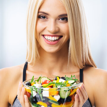 Portrait image - happy excited smiling beautiful woman holding bowl plate of greece salad with cheese, indoors. Blond girl at keto ketogenic dieting, weight loss, healthy eating concept.