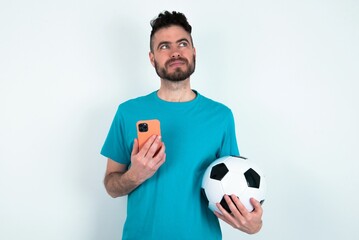 Young man holding a ball over white background holds mobile phone uses high speed internet and...