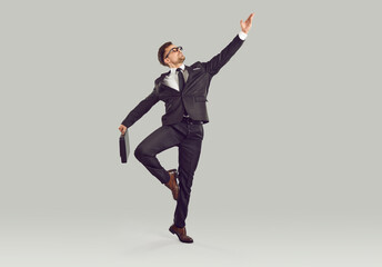 Agile energetic office worker dancing isolated on grey background Full body length shot young business man in classic suit and tie holding diplomat case and doing graceful pirouette like ballet dancer
