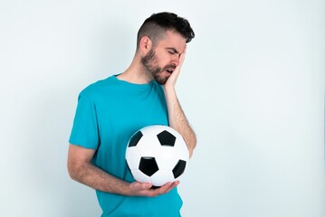 Young man holding a ball over white background with sad expression covering face with hands while...