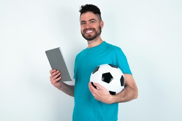 Photo of optimistic Young man holding a ball over white background hold tablet