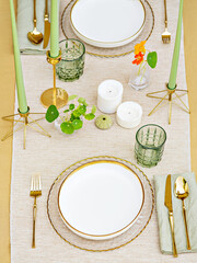 An elegant background photo. A play of beige and green colors brings spring lightness. The fancy table layout with golden cutlery and candles create the setting for an anniversary or a romantic lunch.