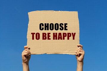 Choose to be happy text on box paper held by 2 hands with isolated blue sky background. This message board can be used as business concept about choosing to be happy.