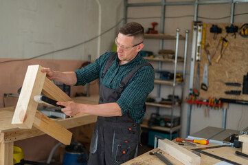 The carpenter shakes off sawdust from a wooden product. 