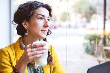 Woman looking through a window with coffee in her hand