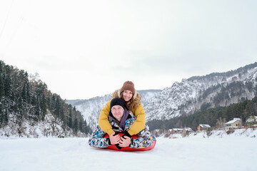 Fototapeta na wymiar Couple having fun on winter vacation, tube in snow, while spending time outdoors on snowy winter day in mountains