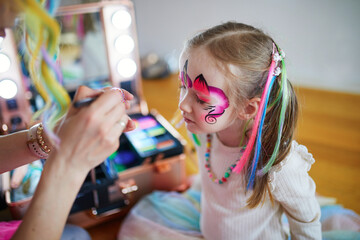 Artist painting little preschooler girl like unicorn on a birthday party