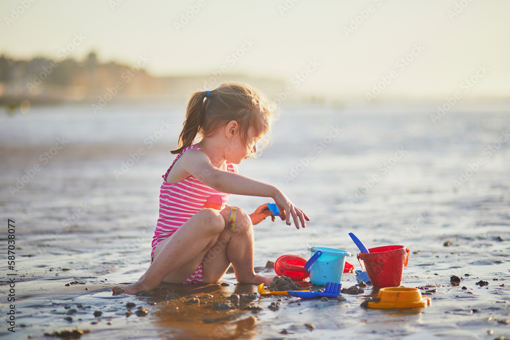 Wall mural preschooler girl playing on the sand beach at atlantic coast of normandy, france