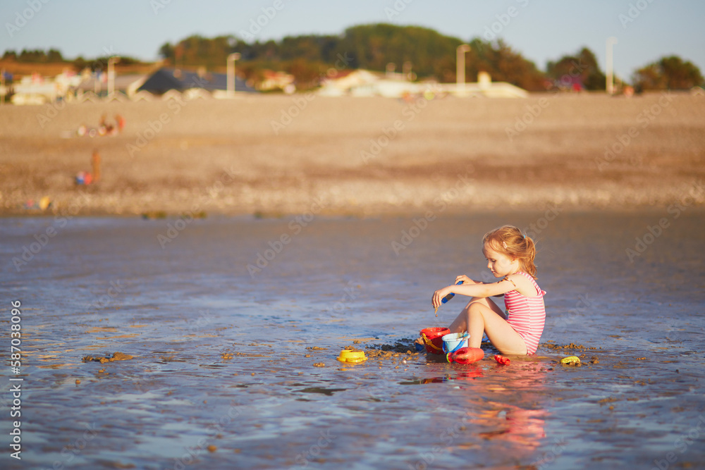 Wall mural preschooler girl playing on the sand beach at atlantic coast of normandy, france