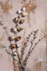 Table Easter decor set with quail eggs, green ribbon and willow branches on wooden vintage table.