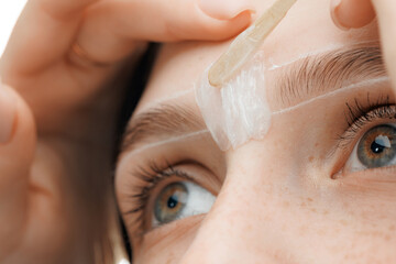 Correction Eyebrow hair waxing. Master combs eyebrows of woman in beauty salon