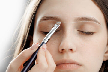 Master draws white guide lines for correction eyebrow of woman in beauty salon