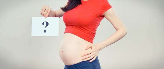 Pregnant woman holding card with question mark. Expecting birth of boy or girl. Extending family. Motherhood