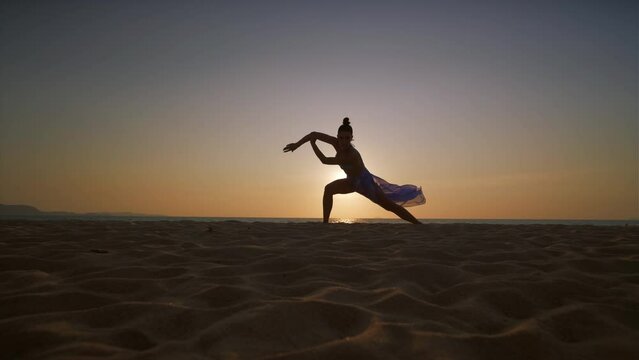 A young woman dancing on the beach at sunset.